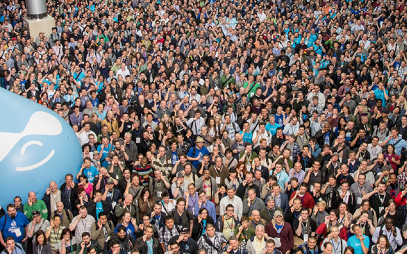 Large crowd gathered outdoors, many smiling, with a giant blue teardrop-shaped balloon.