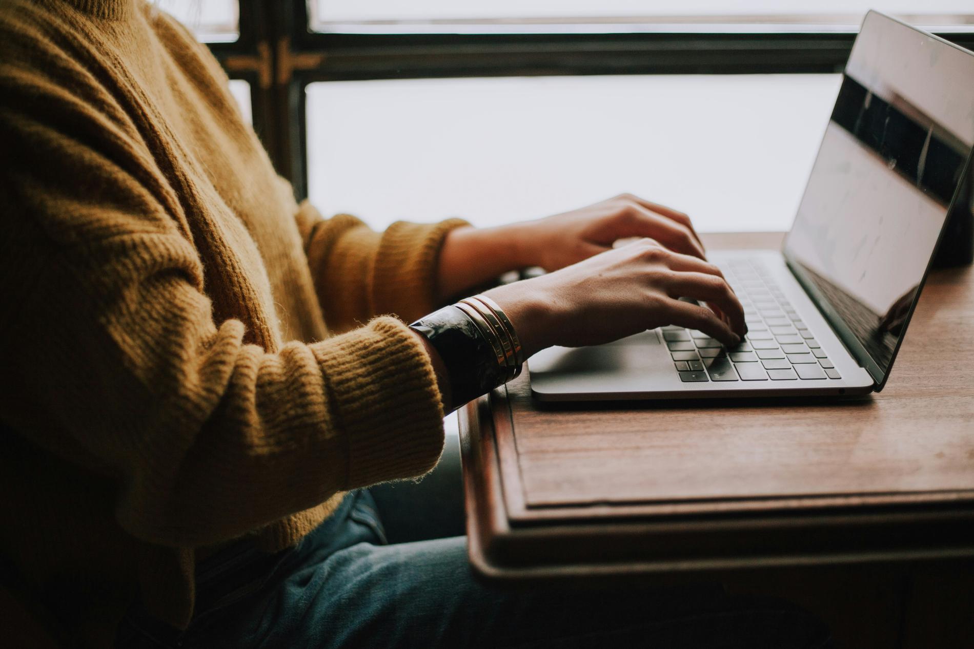 Person typing on a laptop at a wooden desk.