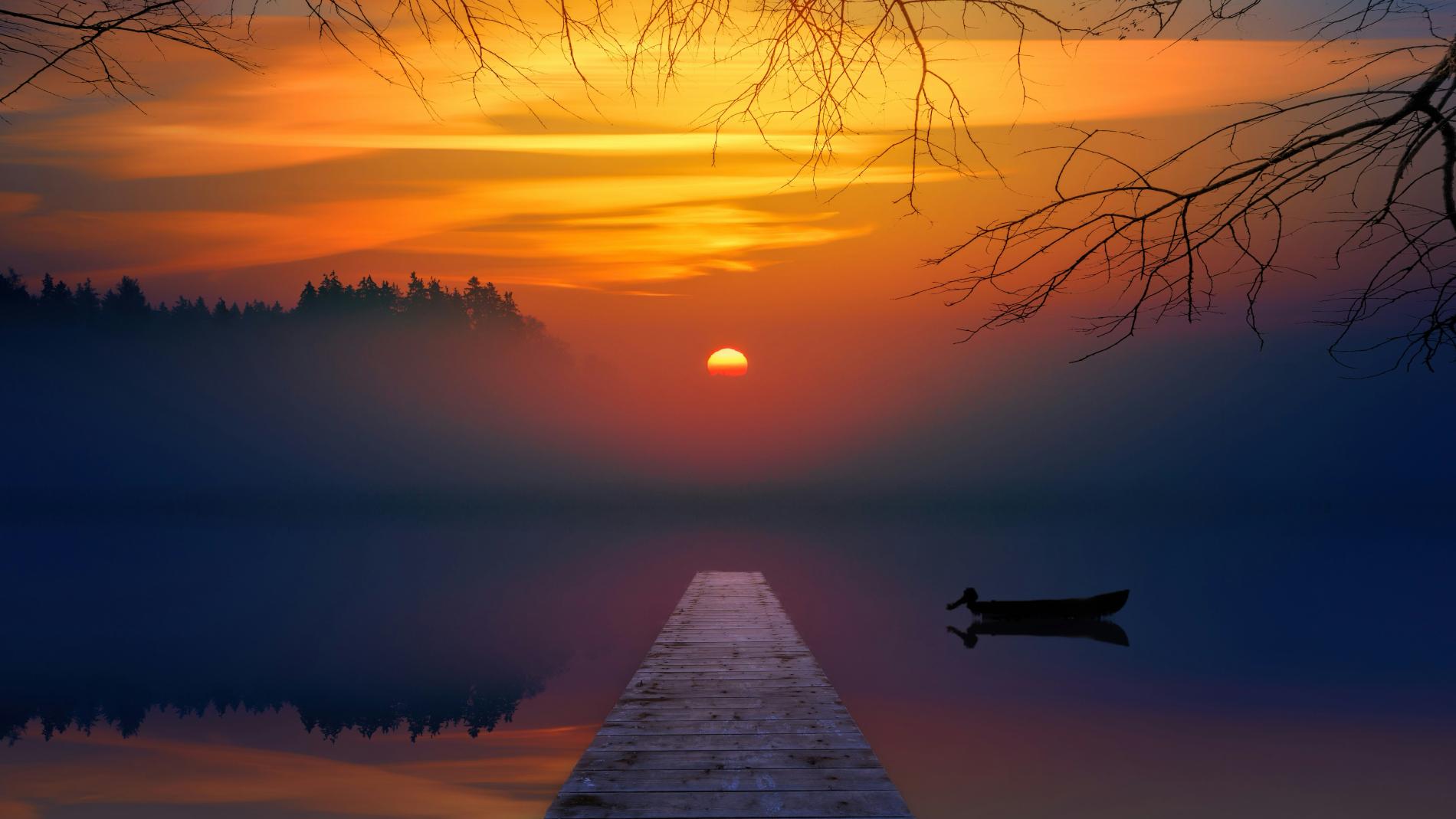 Sunset over a serene lake with a pier and silhouetted boat, hues of orange and blue.