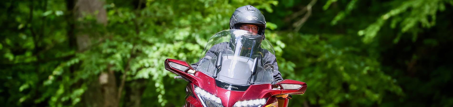Motorcyclist on red bike rides through a lush forest road.